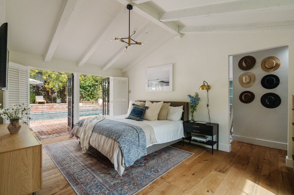 Vaulted primary bedroom with exposed beams and shuttered doors to the pool
