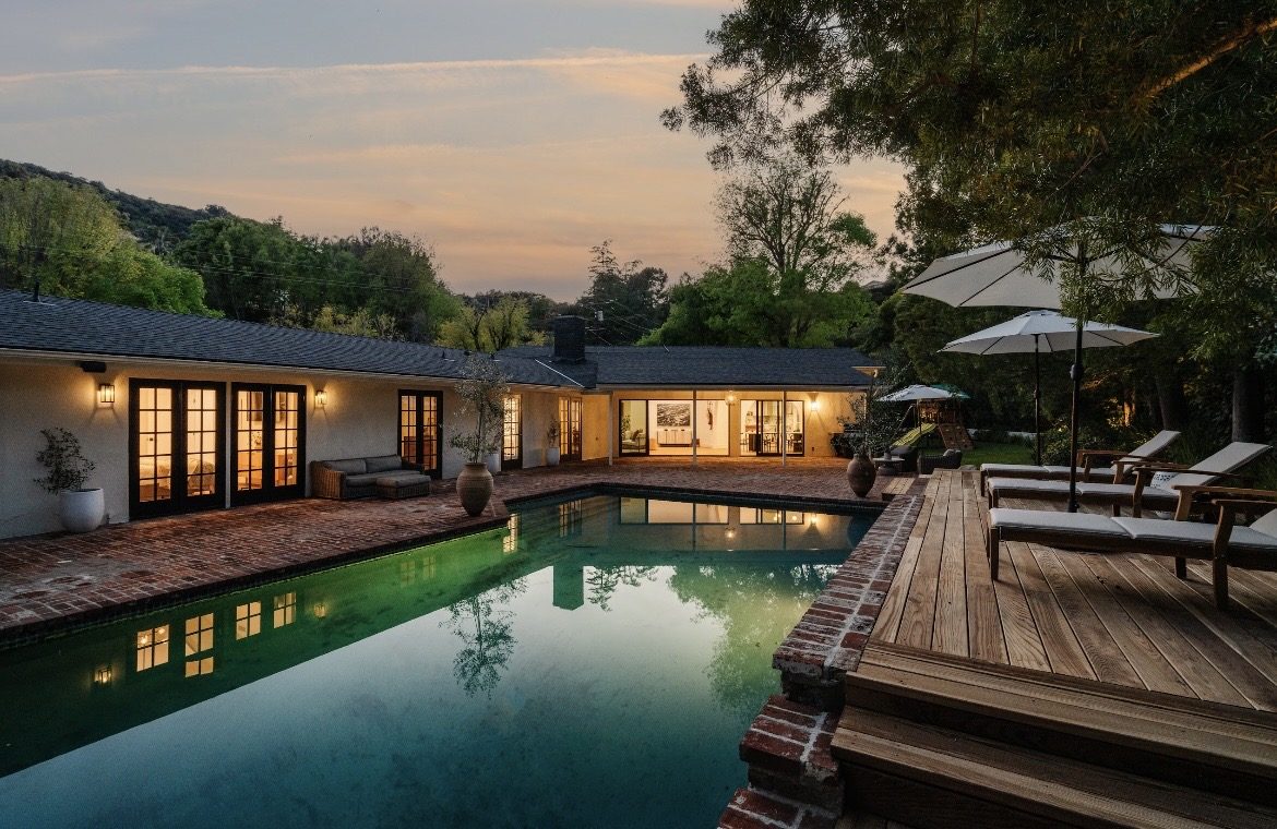 D&H Contractors renovated Encino home at dusk: lit French doors, brick pool terrace and wood deck