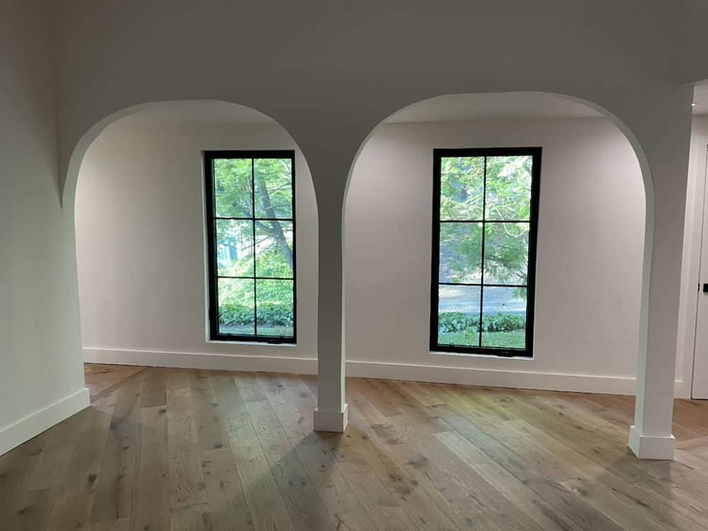 Twin arched black steel windows in a freshly plastered room with oak floors