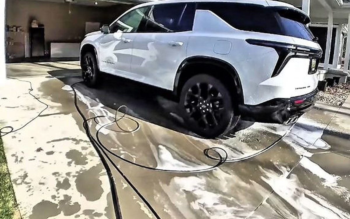 Our mobile rig in a driveway, pressure washer, hoses and water tank out while washing a white SUV: the same setup we bring to the hangar