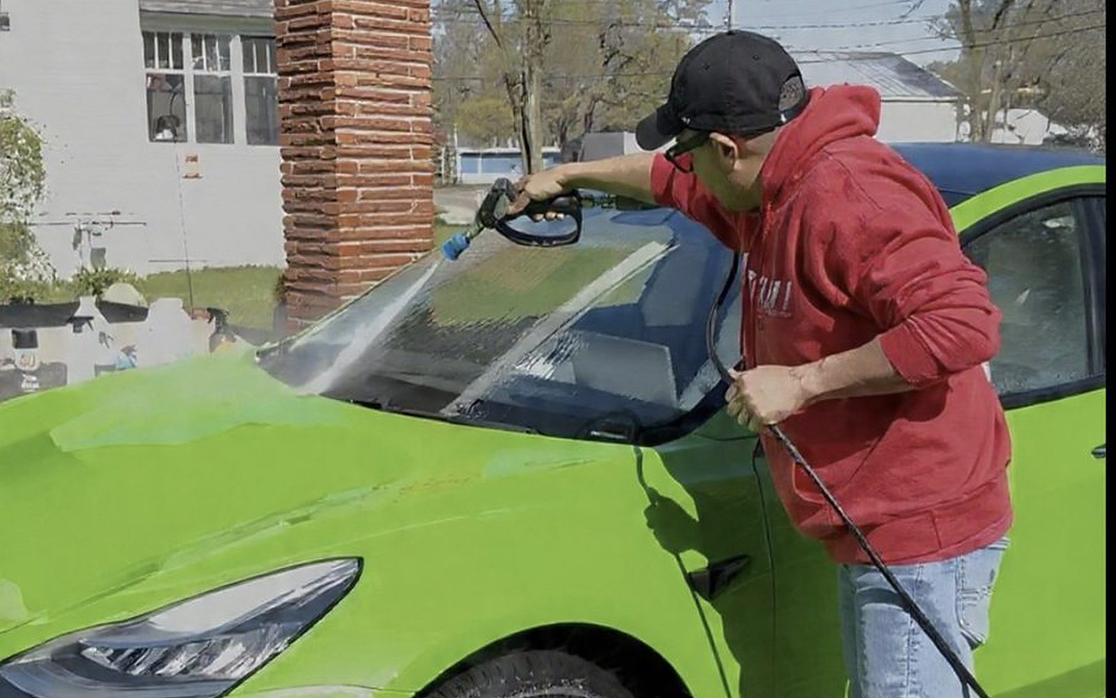 Manrique pressure-washing a lime-green Tesla Model 3 in a driveway, the decontamination wash before ceramic coating
