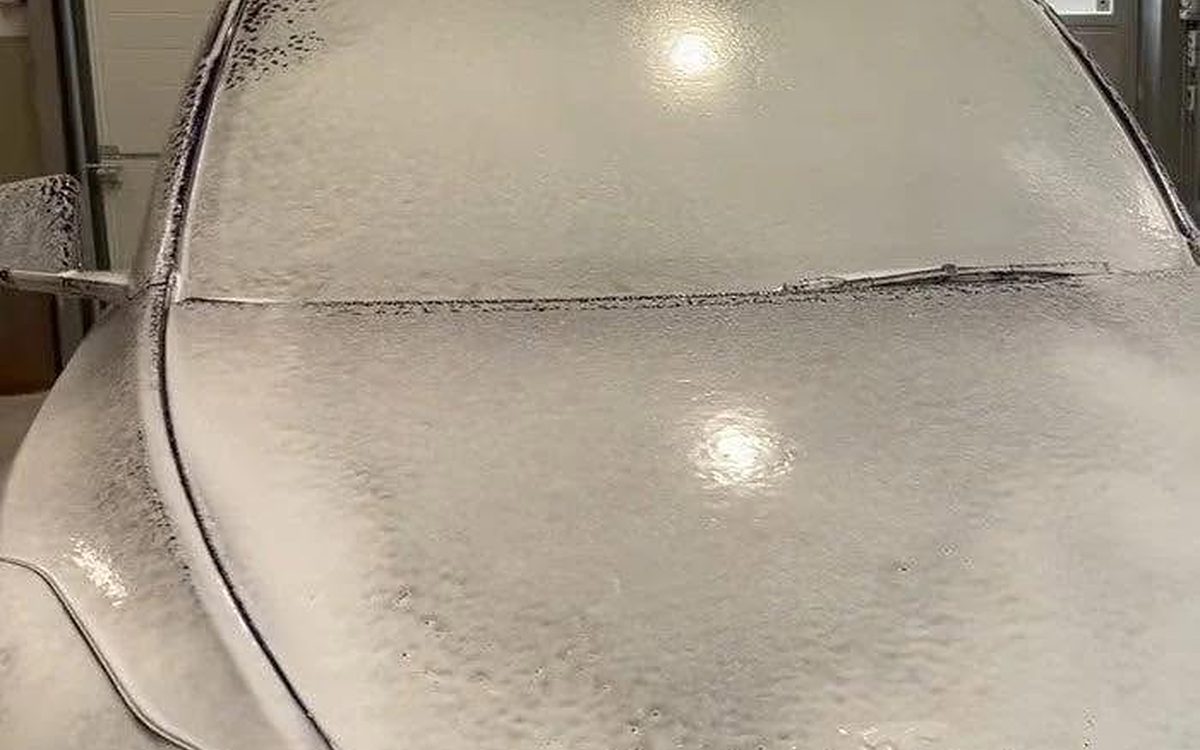 Snow foam covering a car’s hood and windshield during a hand wash in a garage