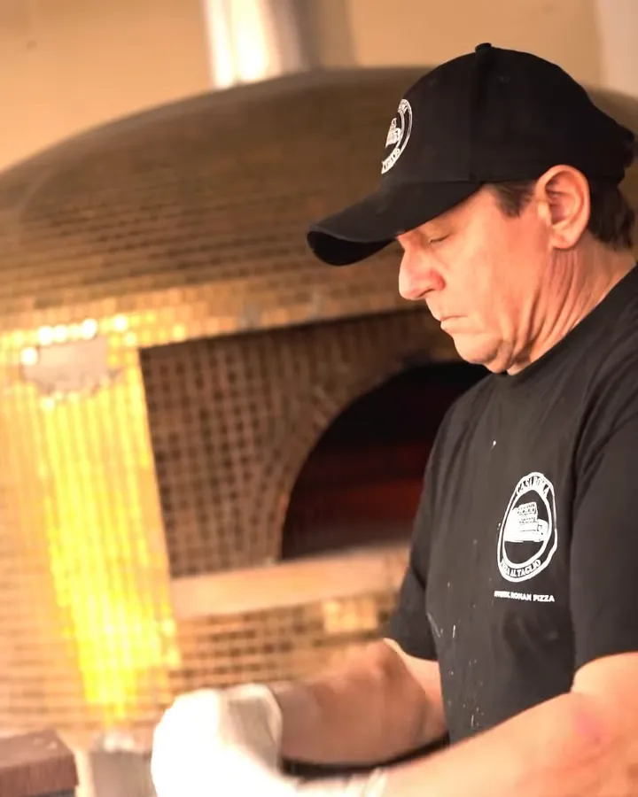 Claudio Alicandri stretching dough in front of a gold mosaic wood-fired oven