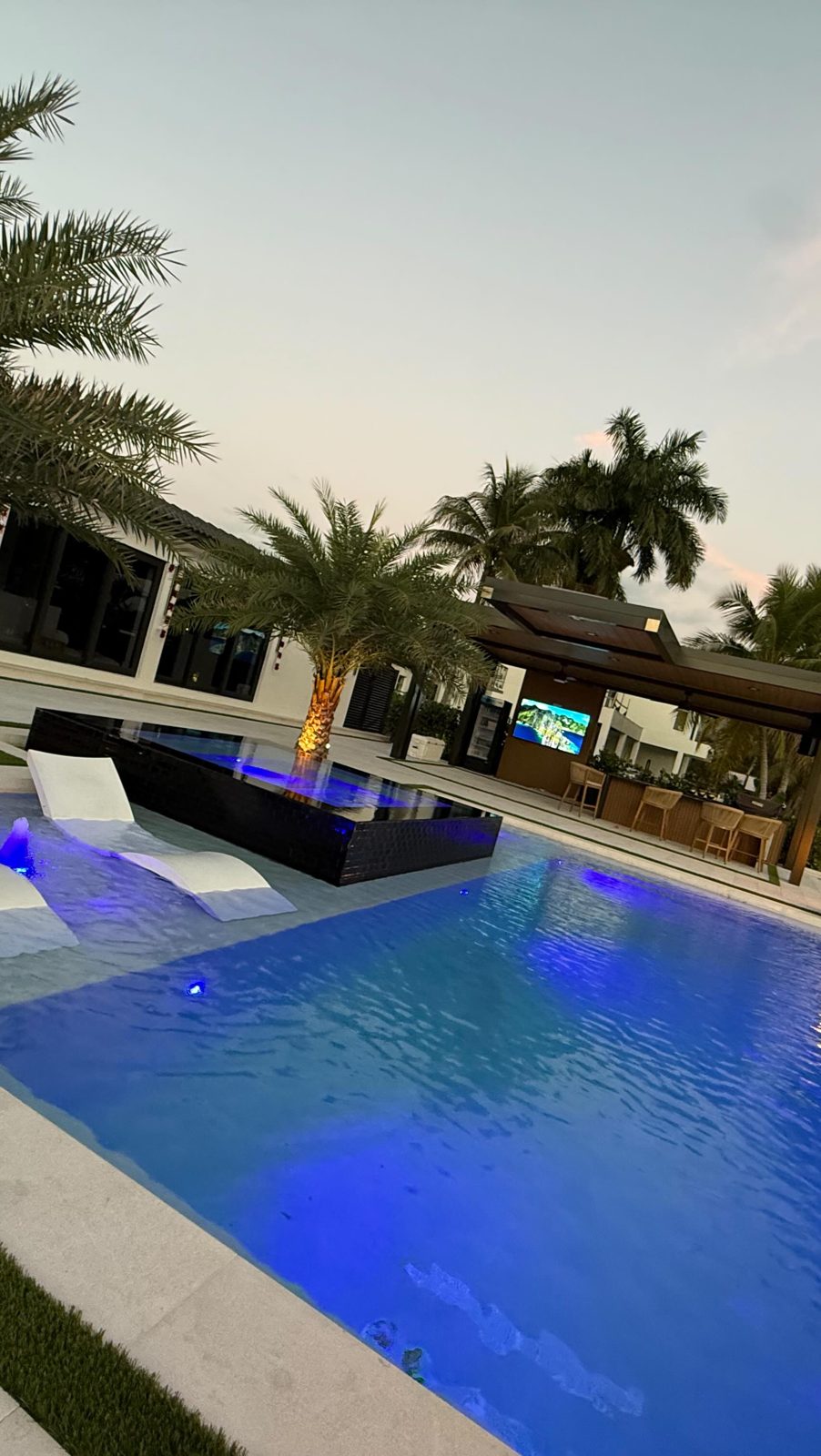 Backyard pool with lighting and covered patio at dusk