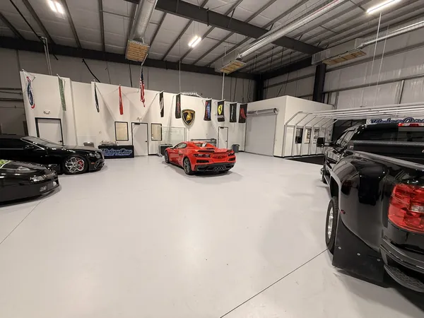 Vista amplia del taller con un Corvette rojo, carros negros y banderas en la pared