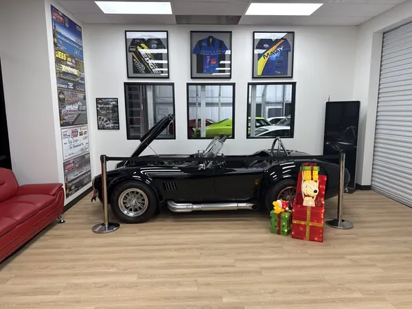 Sala de clientes con un Shelby Cobra, camisetas enmarcadas y un sofá rojo