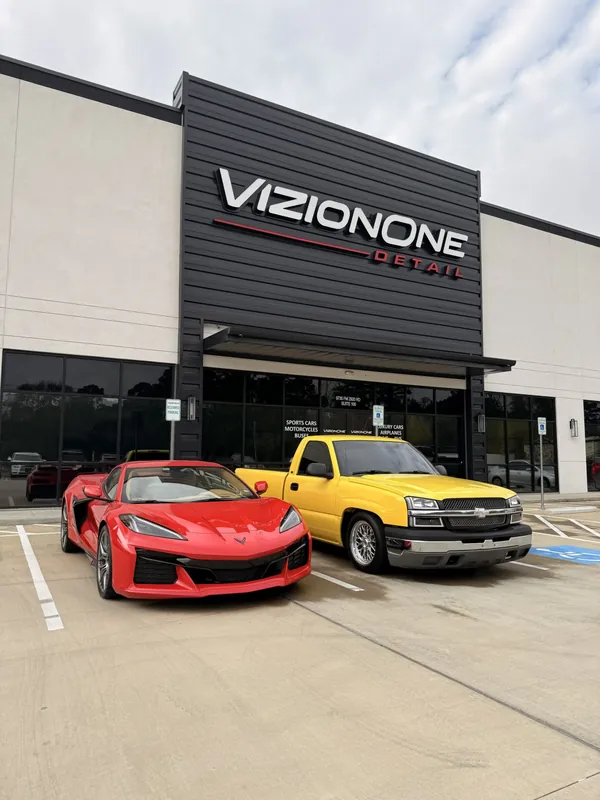 Un Corvette rojo y una troca Chevy amarilla afuera del taller