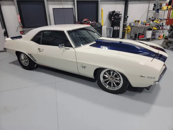 Camaro blanco de primera generación con franjas azules en el taller