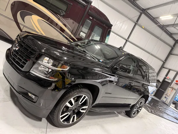 Chevy Tahoe negra en el taller con una casa rodante atrás