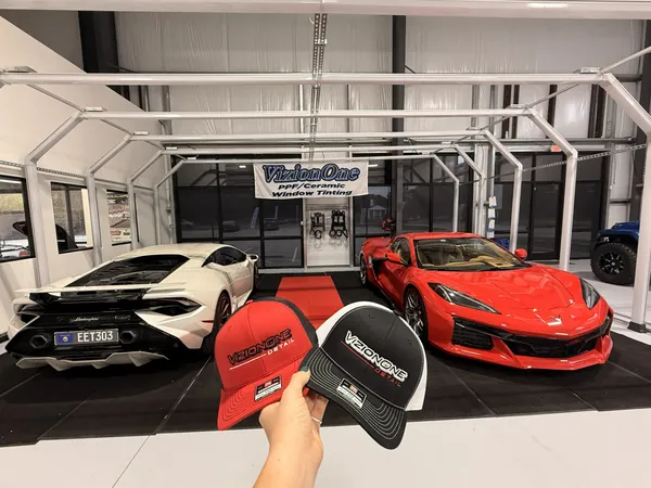 Gorras VizionOne roja y negra, con un Huracán y un Corvette en el taller
