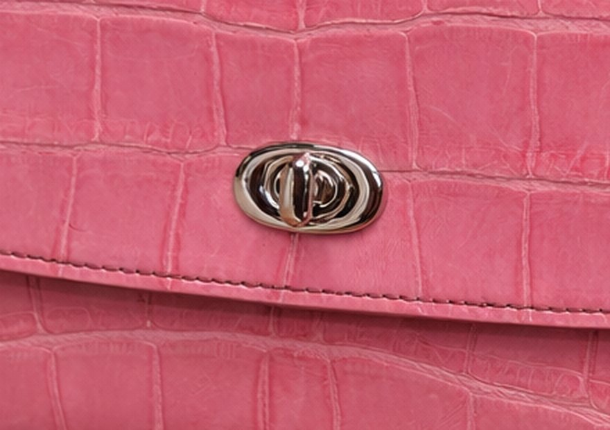 Macro view of the polished turn-lock closure on rosé alligator leather